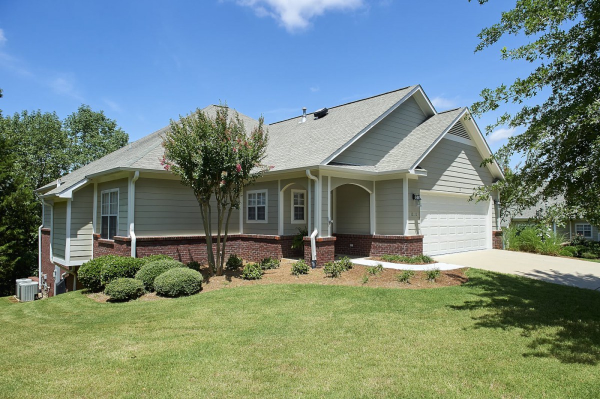 A single-story suburban house with a well-maintained lawn and trees under a clear blue sky.