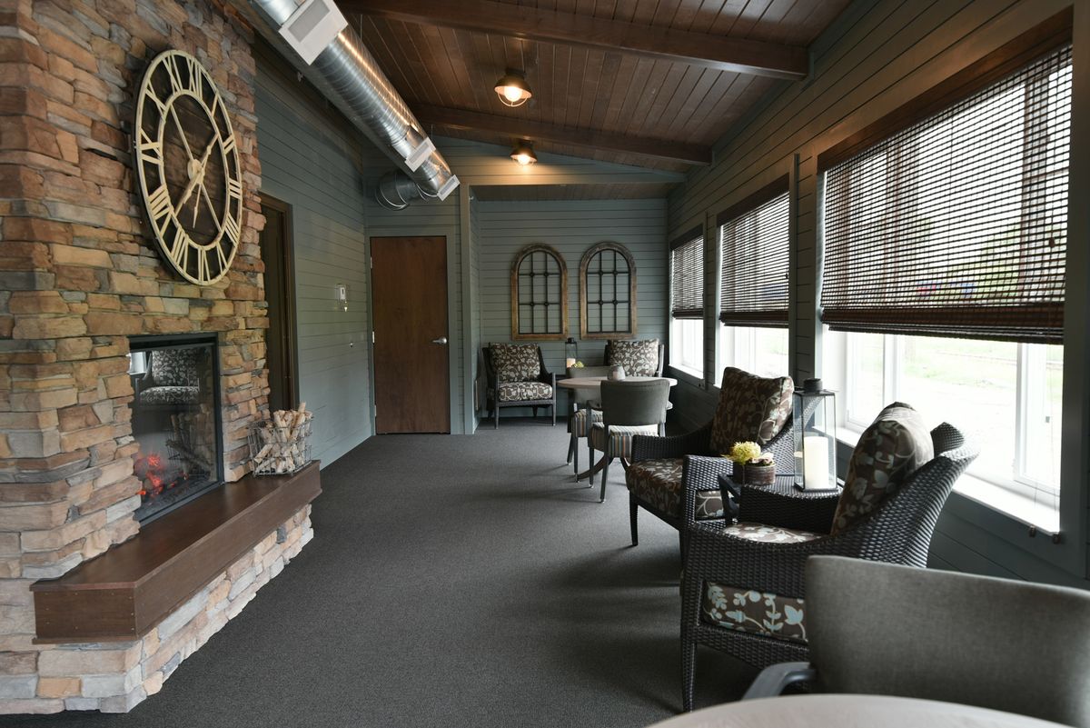 A cozy living room featuring a fireplace with a decorative clock, accompanied by comfortable seating and large windows.