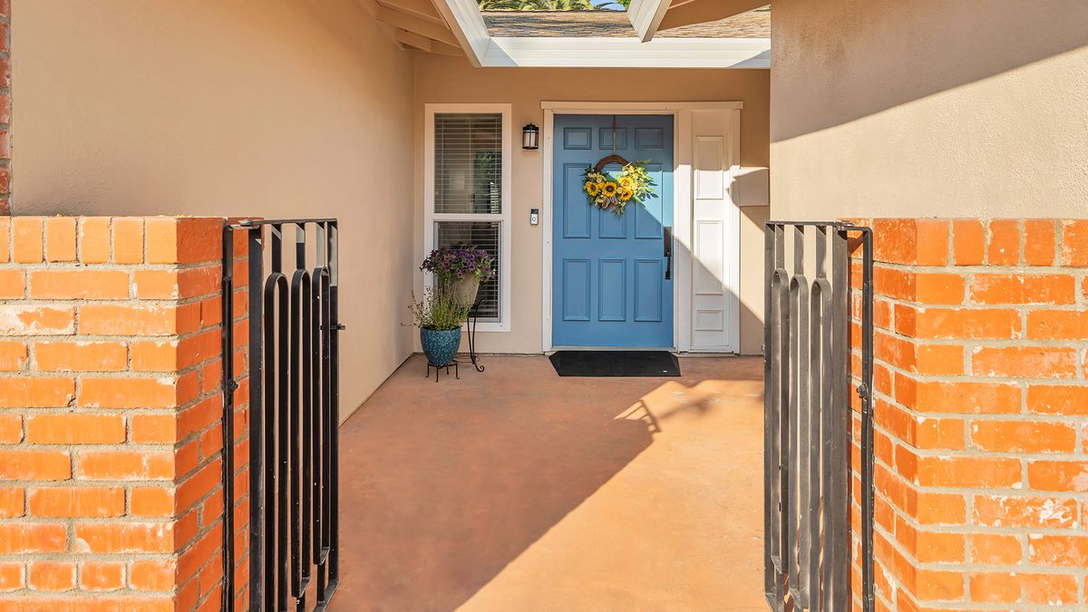 A welcoming porch with a blue front door adorned with a wreath, accompanied by a potted plant and a skylight above.