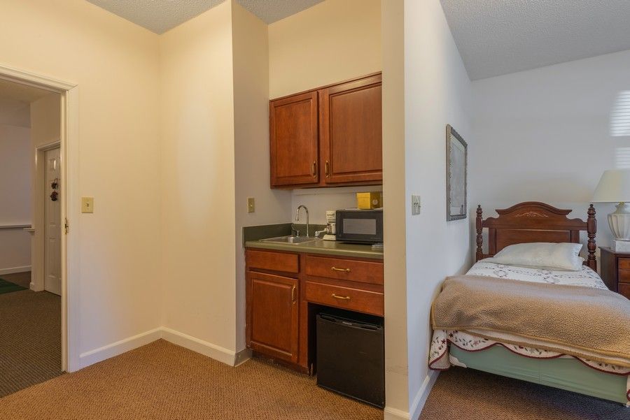 A small kitchenette with a sink, microwave, and mini fridge next to a bedroom.