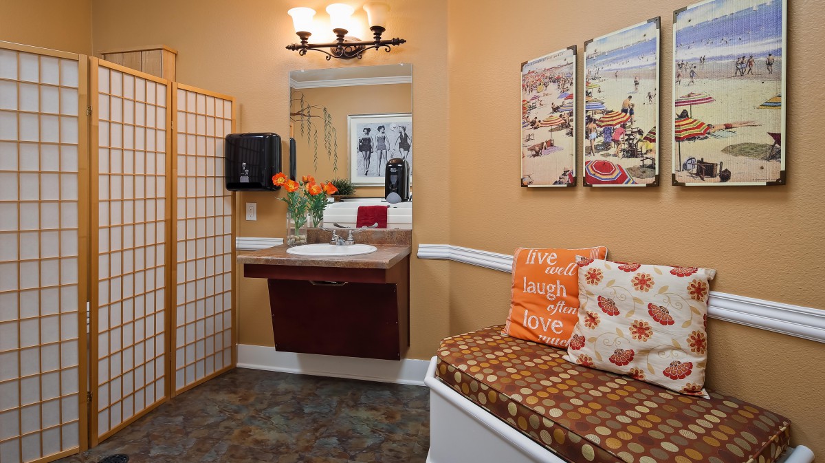 A cozy bathroom featuring a wall-mounted sink, decorative mirror, and comfortable seating with colorful cushions.
