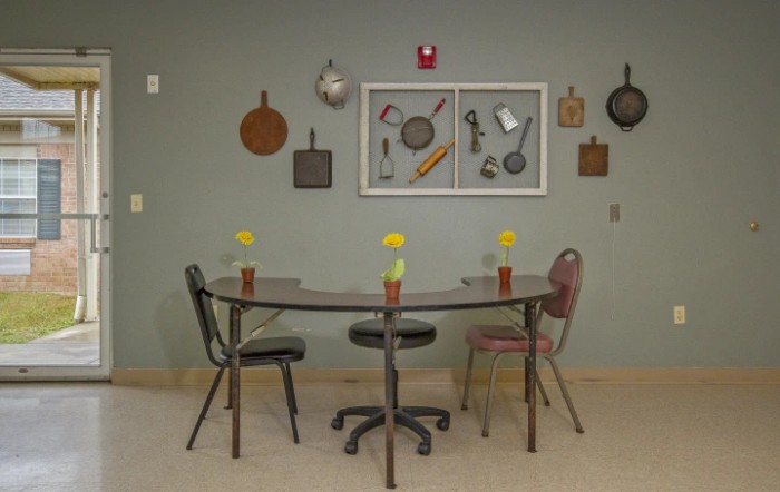 A quaint kitchen dining area with a table and mismatched chairs, adorned with wall decorations featuring vintage cooking utensils.