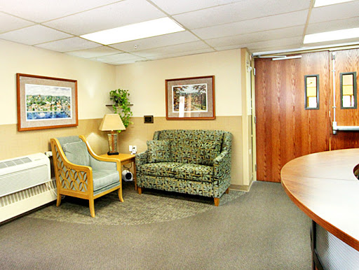 A cozy waiting area featuring a sofa and chairs, adorned with artwork and indoor plants.