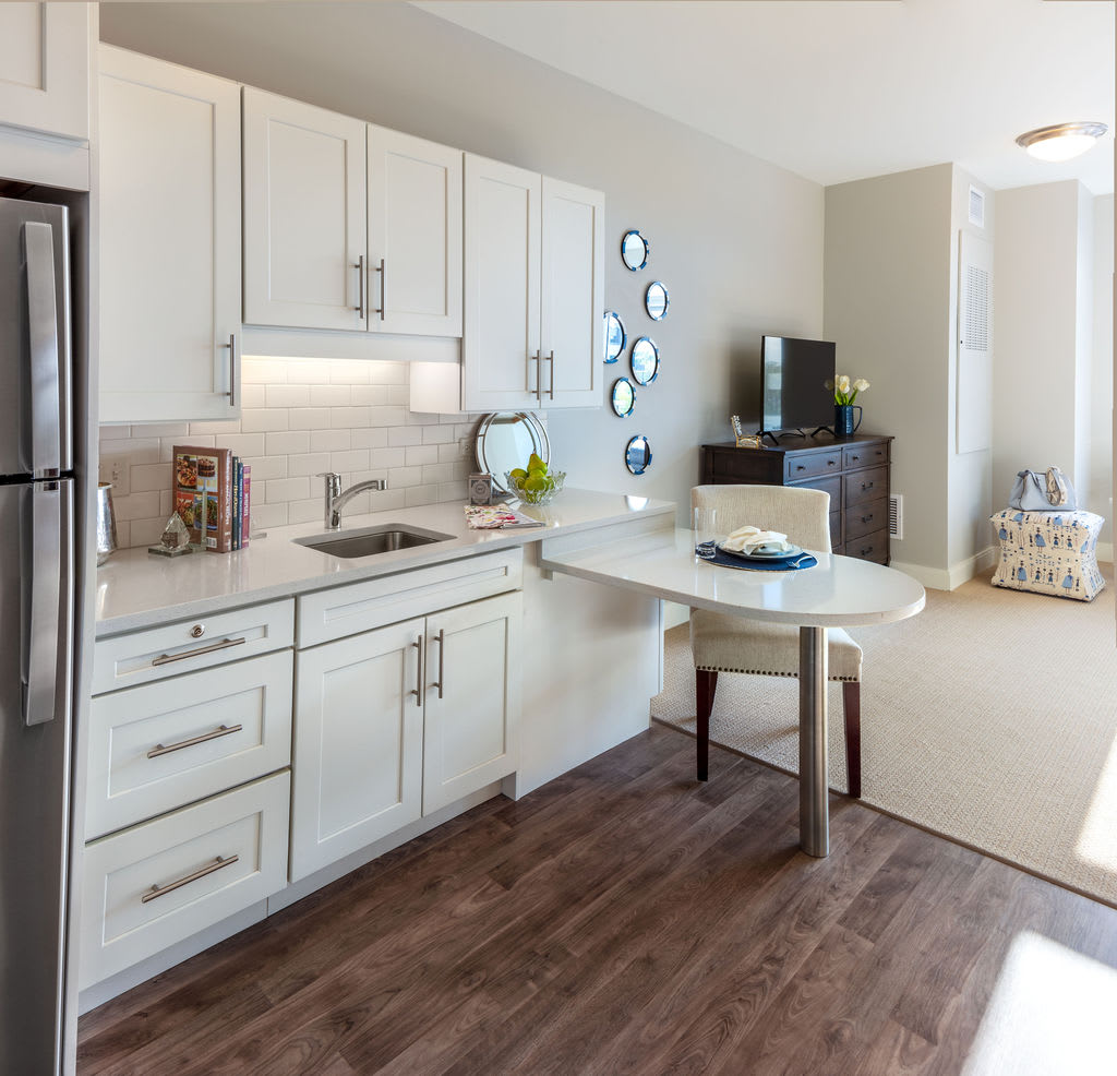 A modern kitchen with white cabinets, wood flooring, and a small dining area.