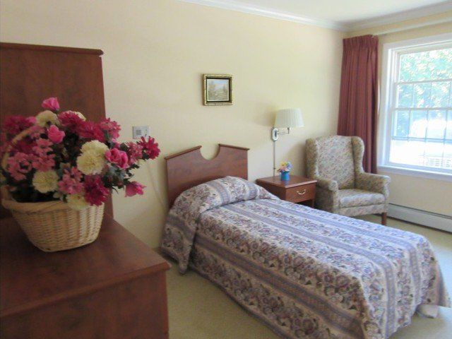 A cozy bedroom with a single bed, an armchair, and a vase of flowers.