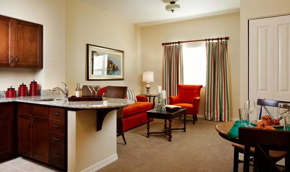 A cozy living room with a red sofa, chairs, and a coffee table, complemented by warm lighting and colorful curtains.
