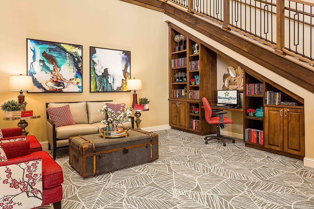 A cozy living room with a sofa, artwork, and a home office setup under the staircase.