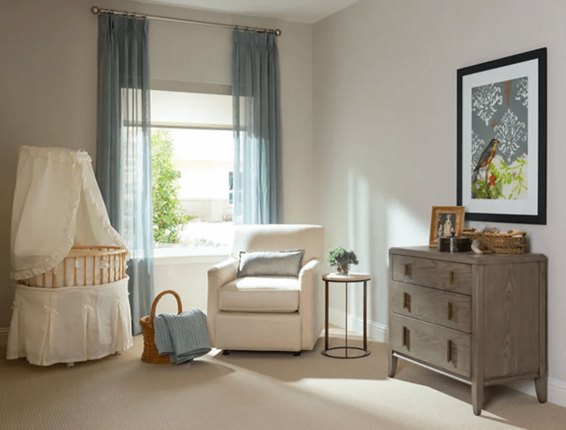 A cozy nursery with a comfortable armchair, a white crib, and a wooden dresser, softly lit by natural light.