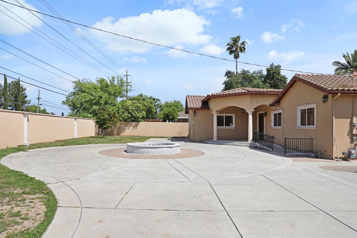 A sunny day in a residential area with a house featuring an arched porch and a spacious concrete driveway.