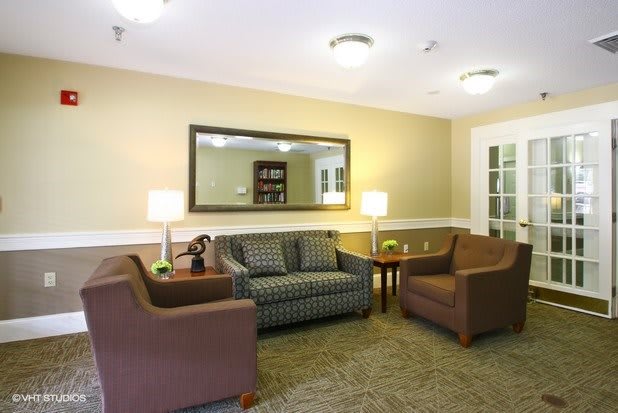 A cozy living room featuring a sofa, armchairs, and a coffee table arranged around a carpet with soft indoor lighting.