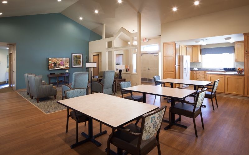 A spacious dining area with tables and chairs, featuring wooden flooring and an open kitchen.