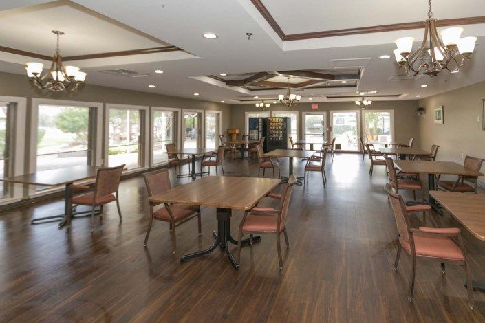 A spacious dining area with wooden floors, large windows, and multiple tables and chairs.