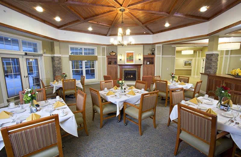An elegantly decorated dining room featuring neatly arranged tables and chairs, a chandelier, and a cozy fireplace.