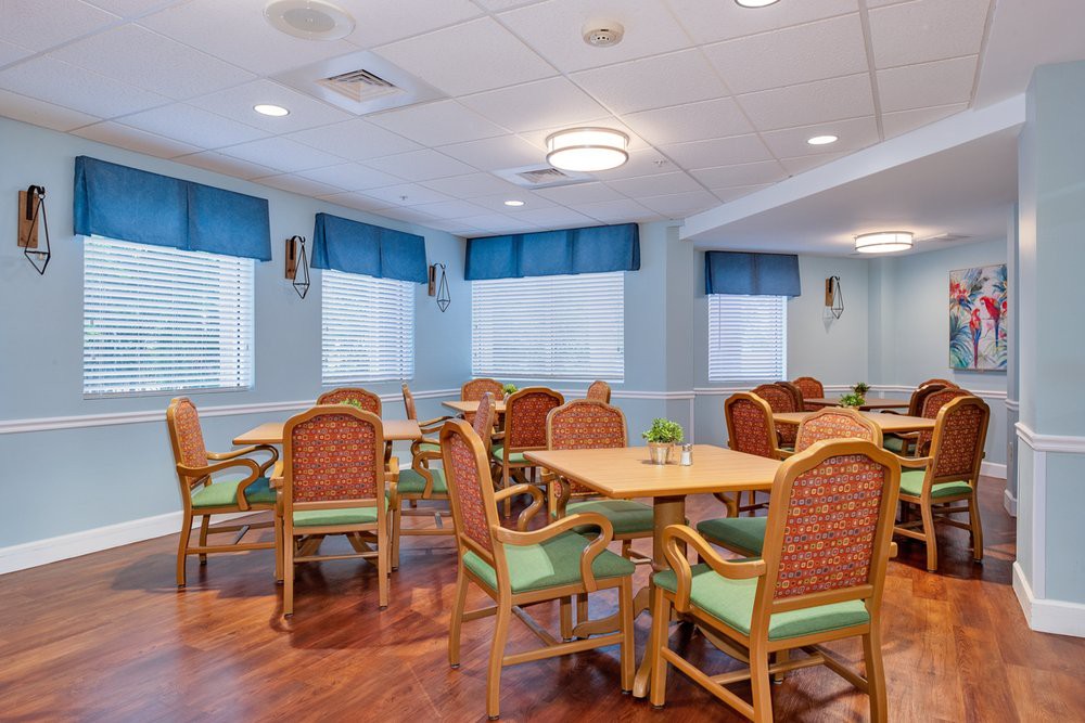 A cozy dining area with several tables and chairs, featuring blue curtains and wooden flooring.
