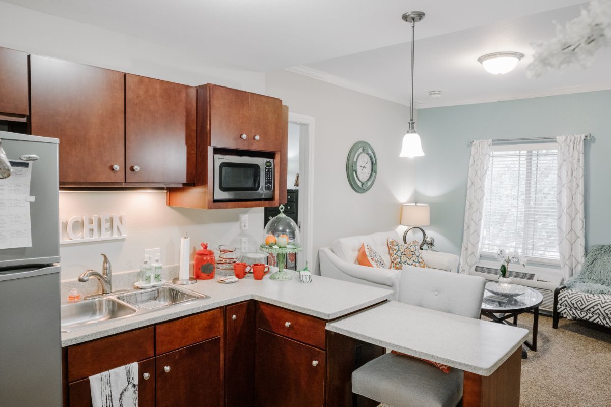 A modern kitchen with wooden cabinetry, a countertop, and pendant lighting, adjacent to a cozy living area.