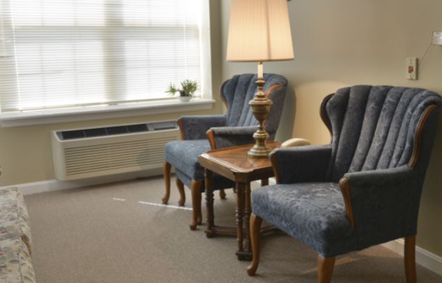A cozy sitting area with two blue armchairs and a wooden table topped by a lamp.