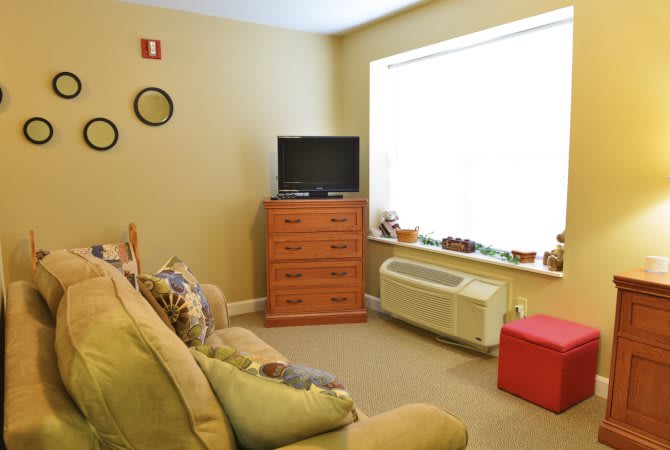 A cozy living room with a sofa, dresser, and television near a large window.