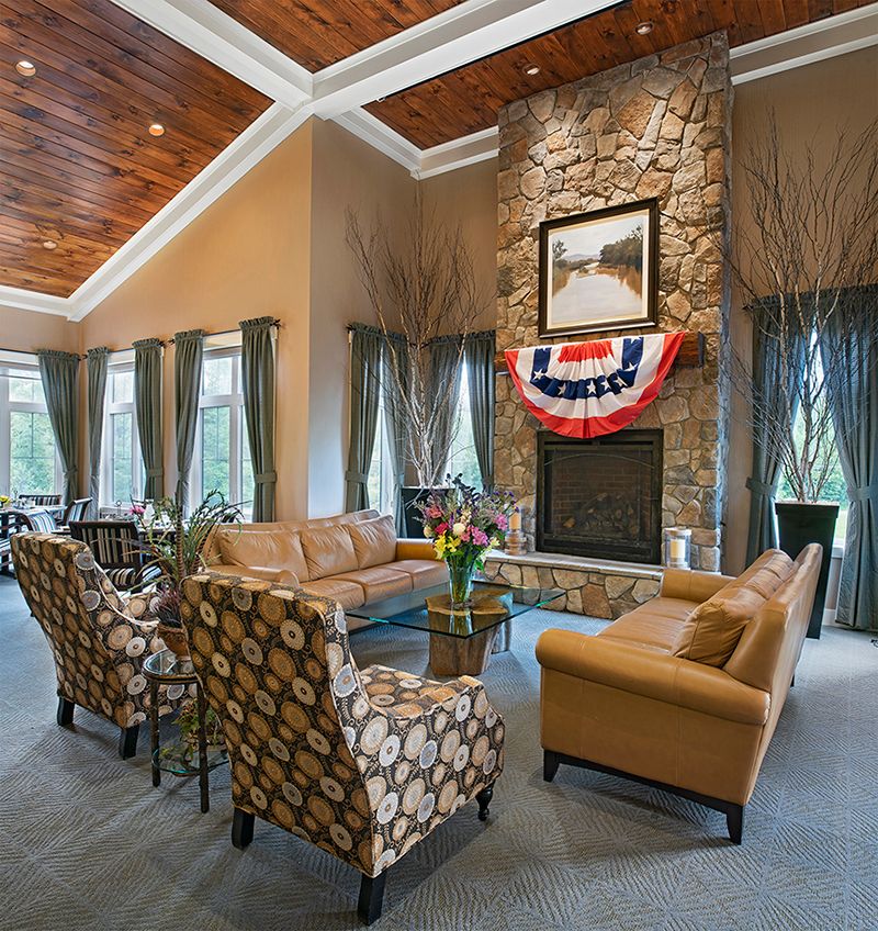 A spacious living room featuring a stone fireplace, leather sofas, and decorative armchairs under a wooden ceiling.