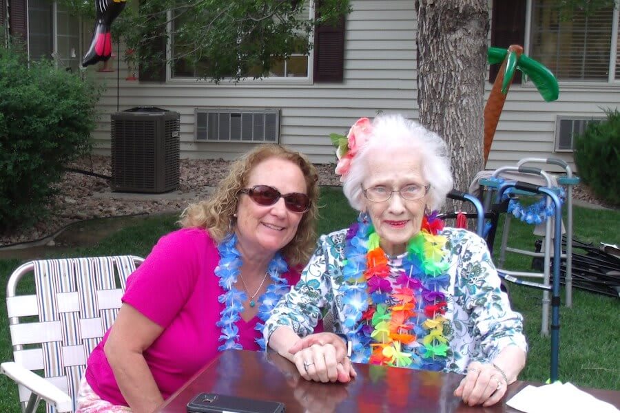 Two women enjoying an outdoor party, wearing colorful leis and smiles.