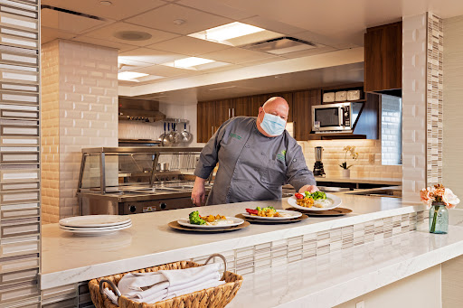 A chef plates dishes in a modern kitchen while wearing a mask.