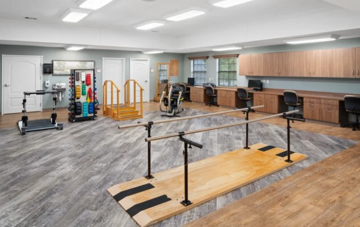 A spacious rehabilitation room equipped with parallel bars, exercise equipment, and therapy tools.