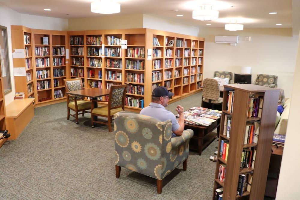 A person sitting in a library, surrounded by bookshelves and reading materials.