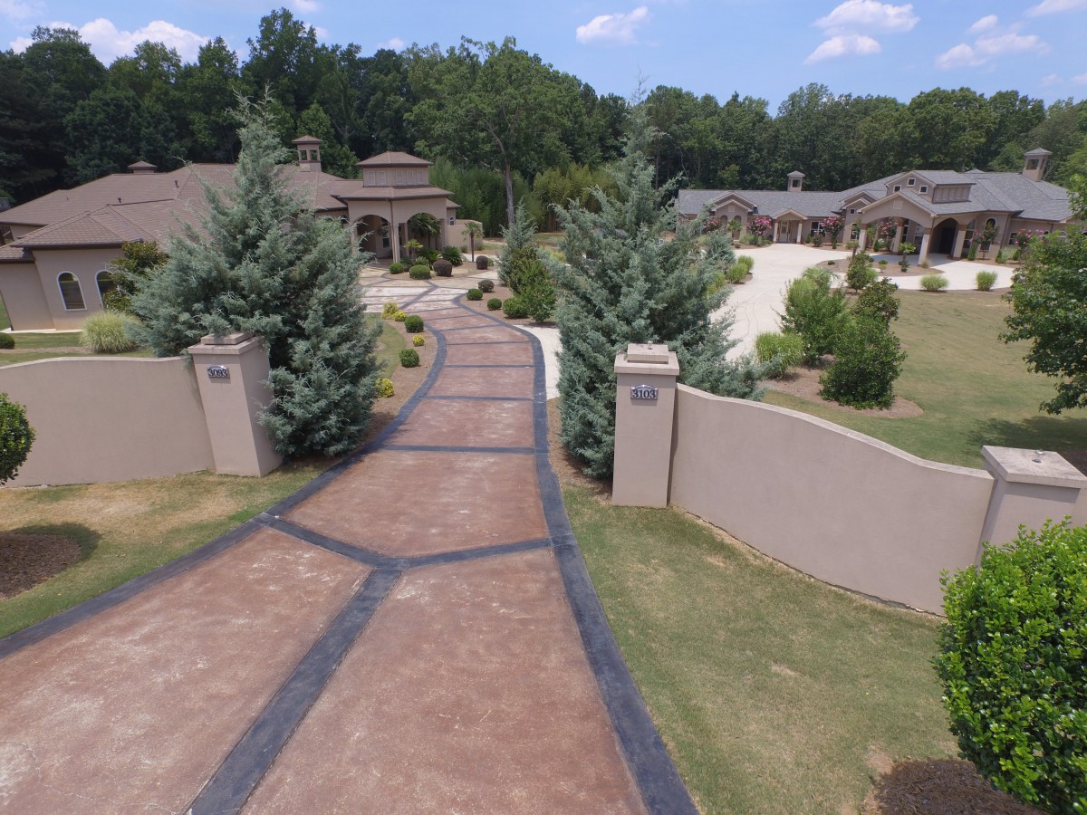 A luxurious driveway leading to a large, elegant home with well-maintained landscaping and a gated entrance.