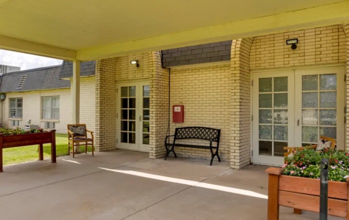 A building entrance with a brick wall features outdoor benches and a covered patio area.