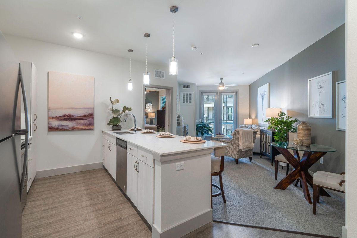 A modern kitchen and dining area with an open floor plan, featuring an island counter and stylish lighting.