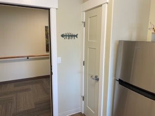 A kitchen corner with a closed door, fridge, and fish-shaped wall decor.