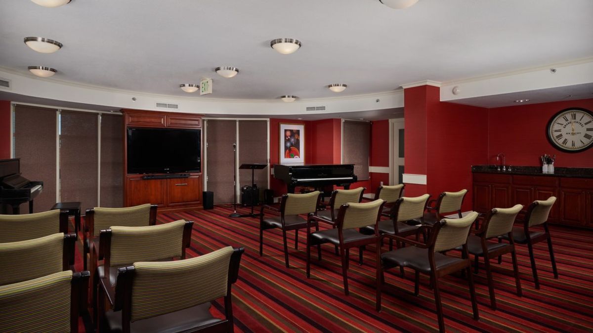 A small conference room with arranged chairs, a piano, and a television.