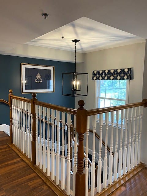 A stylish interior with a wooden staircase and modern chandelier, featuring a window and artwork on the wall.