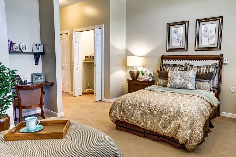 A cozy and elegantly decorated bedroom with a bed, nightstand, lamp, and framed artwork.