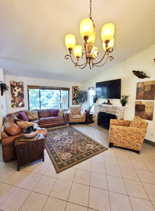 A cozy living room with a sofa, armchair, and fireplace, adorned with a chandelier and decorative elements.