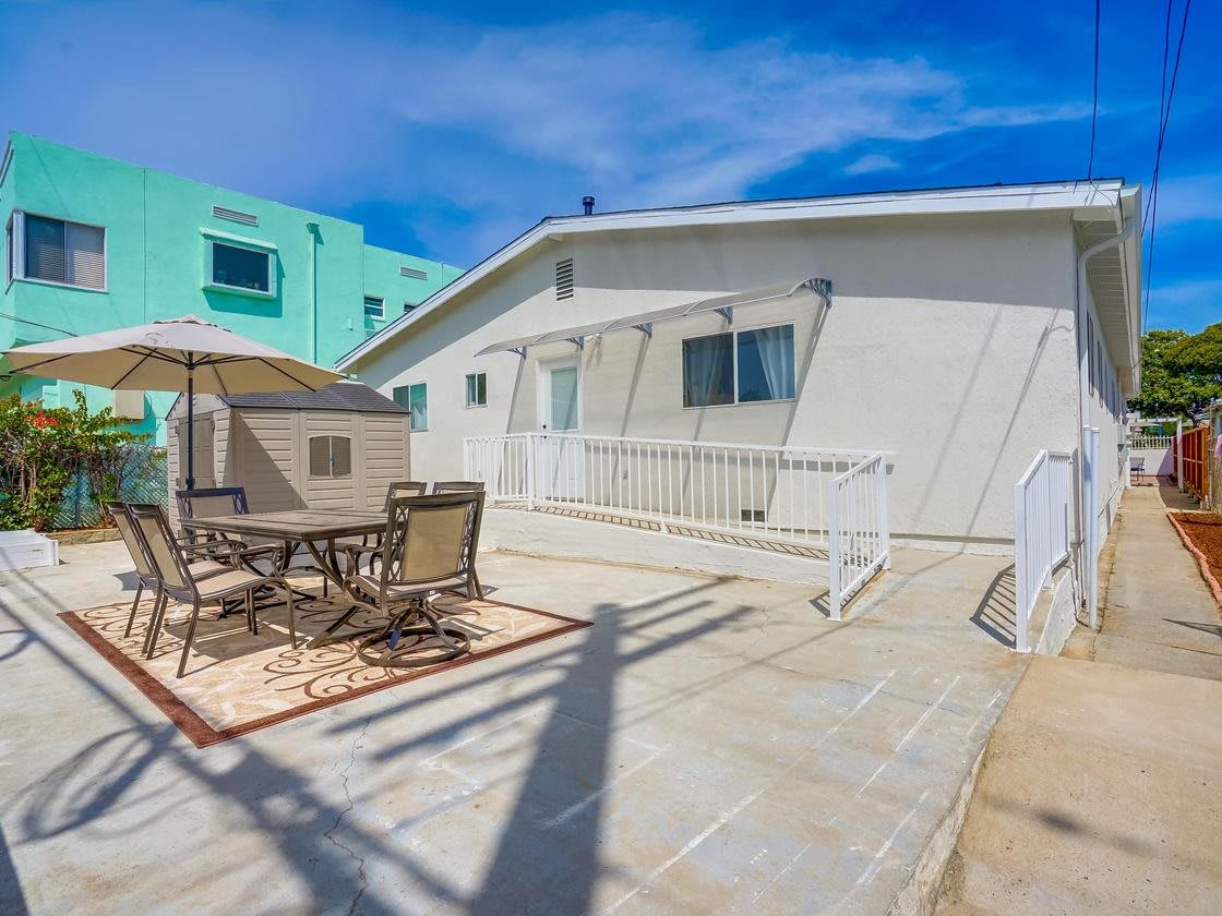 A sunny patio area with outdoor furniture and an umbrella in front of a white house.