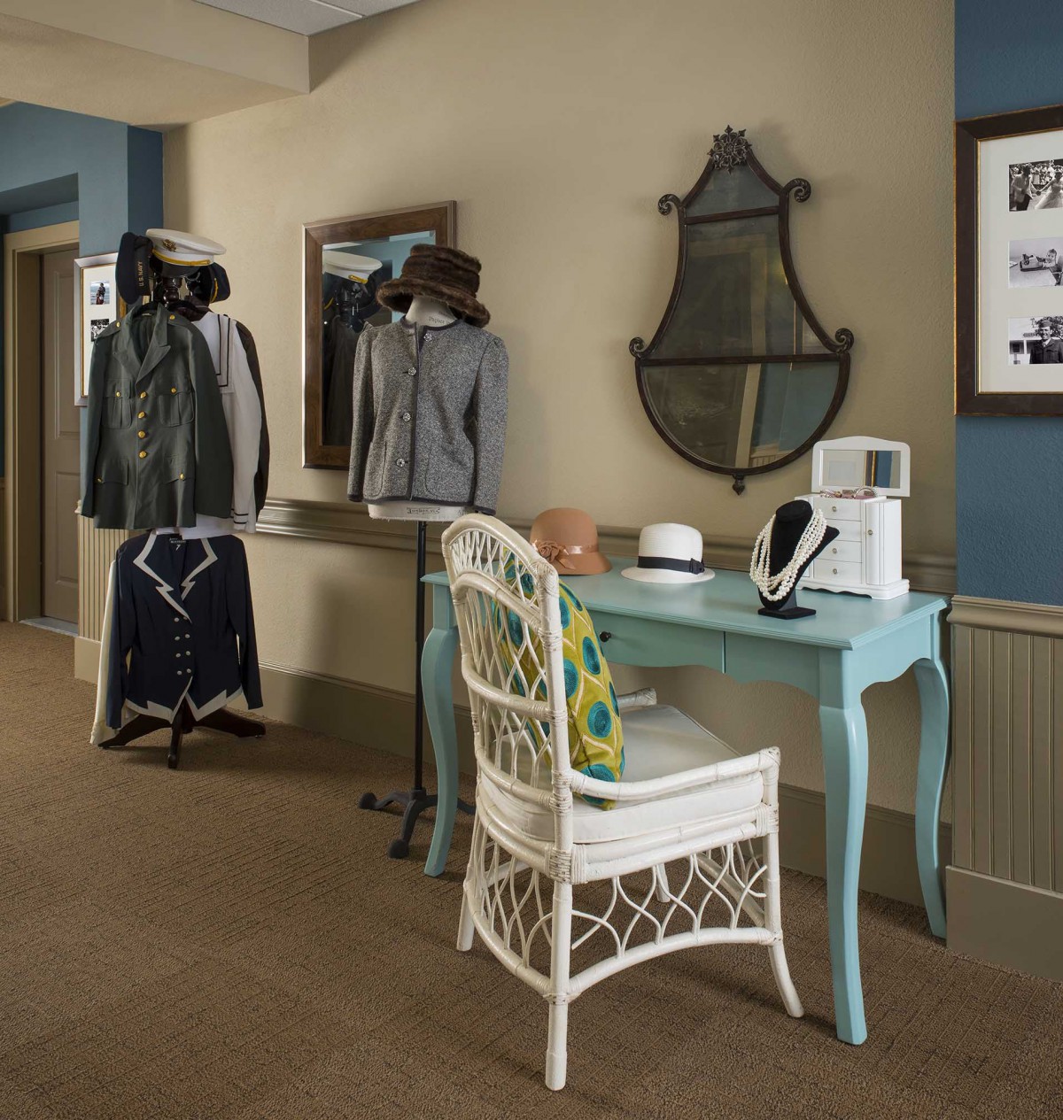 A stylish interior featuring a light blue desk with a mirror above it, accompanied by a wicker chair and nearby clothing rack.