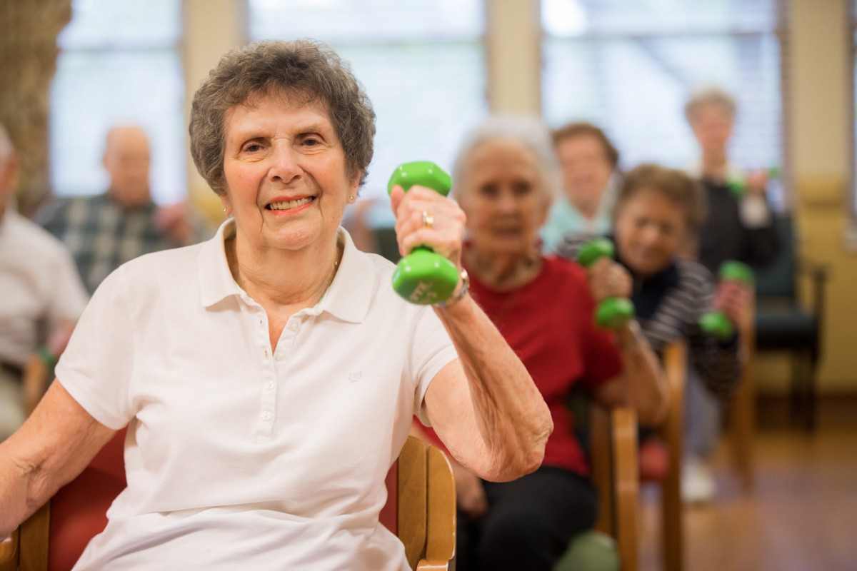 A group of seniors participating in a fitness class, lifting small dumbbells indoors.