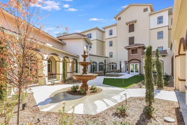 A sunny courtyard with a fountain surrounded by a multi-story building.