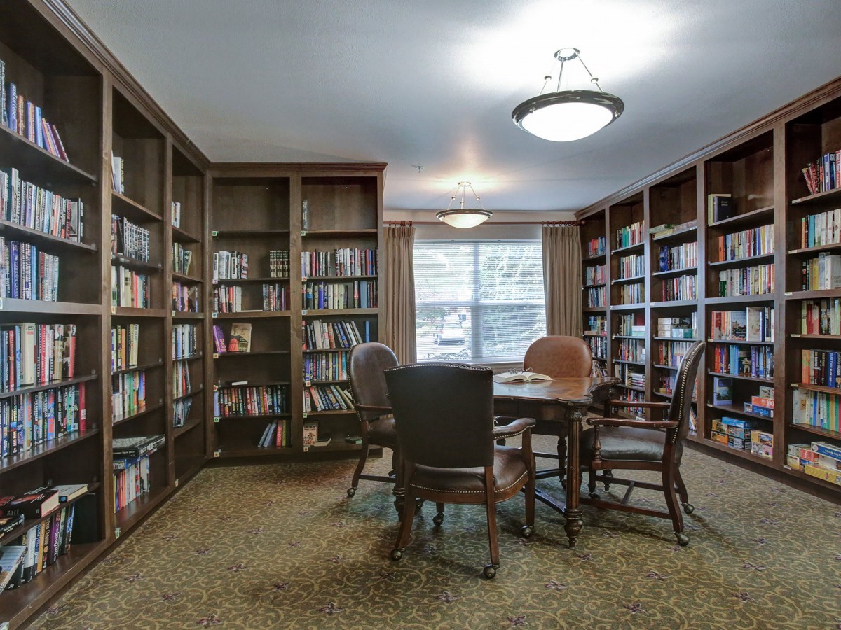 A cozy library reading room with bookshelves lining the walls and a central table surrounded by chairs.