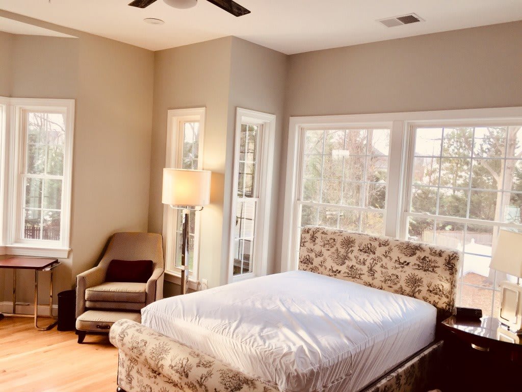A bright and cozy bedroom with a large bed, armchair, and ample natural light streaming through windows.