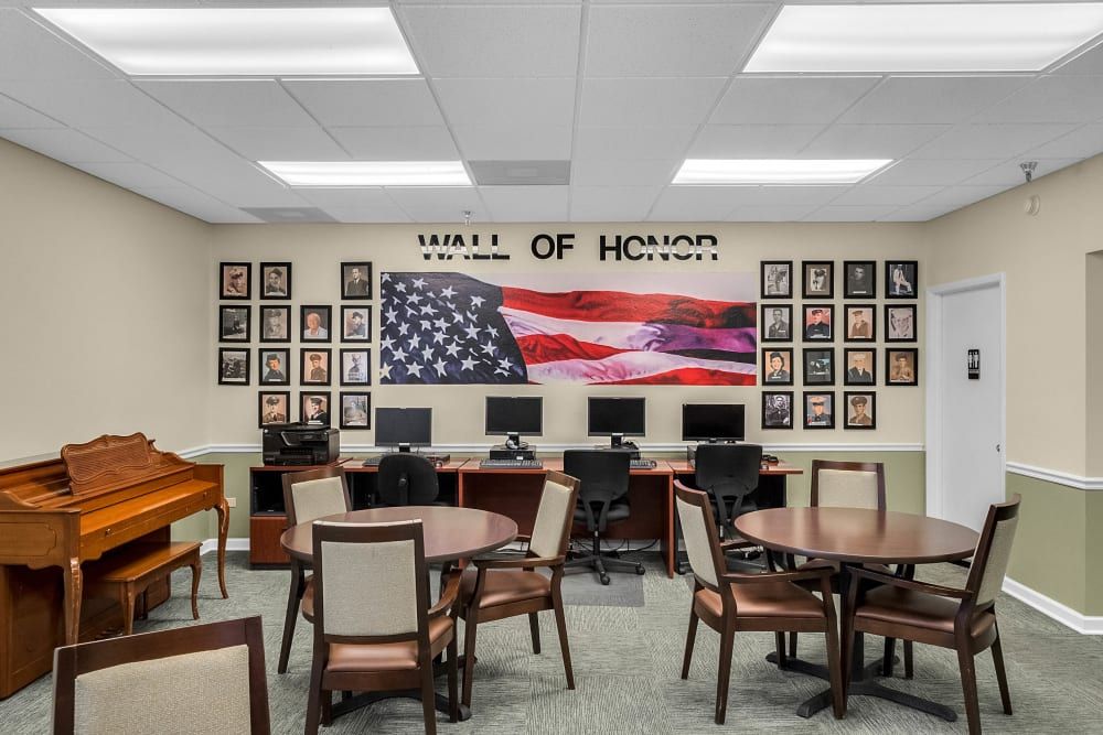 A room featuring a Wall of Honor with photographs, American flag, computers, tables, and chairs.