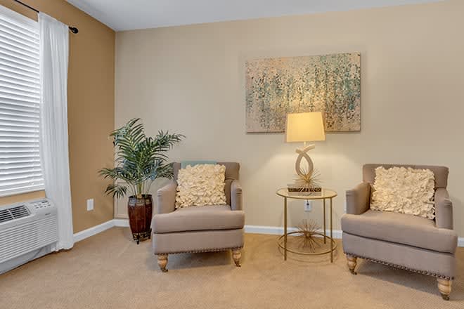 A cozy living room setup featuring two chairs, a lamp on a side table, and decorative artwork on the wall.