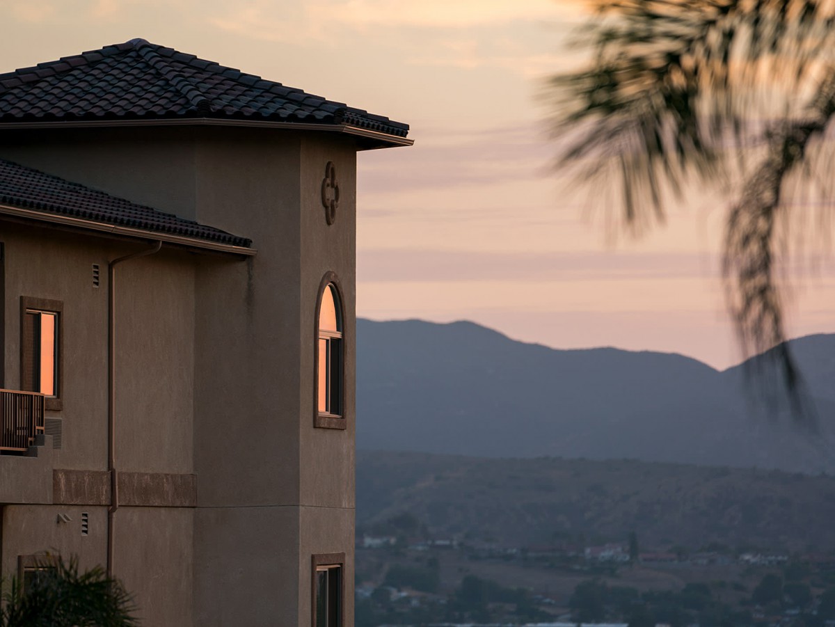 A picturesque view of a house at sunset with mountains in the background.