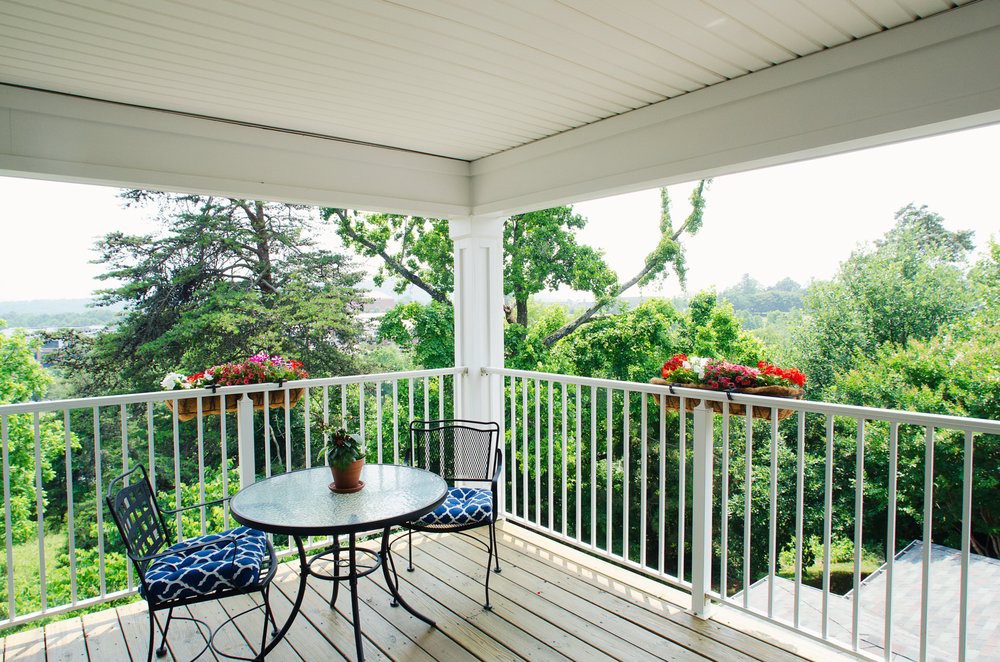 A cozy balcony with a round table and two chairs, surrounded by lush greenery.