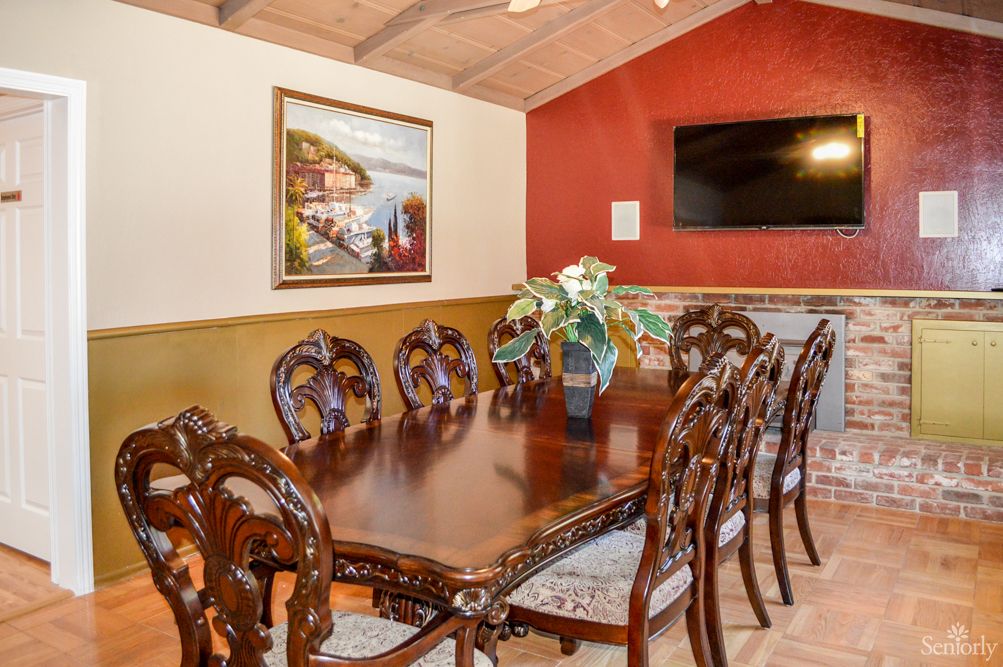 An elegant dining room with a large wooden table and intricately designed chairs, complemented by wall art and a television on red walls.