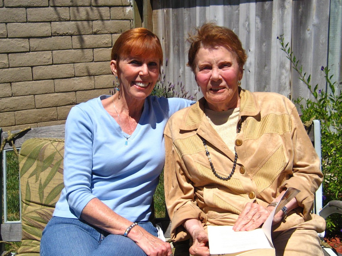 Two women sitting together outdoors, smiling in a sunny setting.