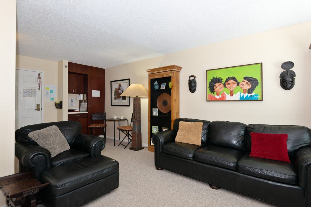 A cozy living room with leather sofas, colorful artwork, and a wooden bookshelf.