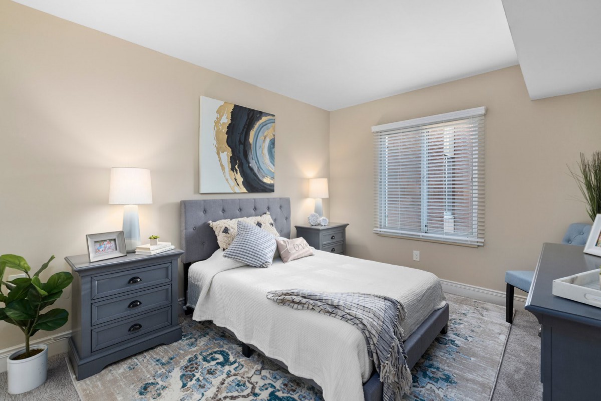 A cozy bedroom with a neatly made bed, elegant nightstands, lamps, abstract artwork on the wall, and a patterned rug.