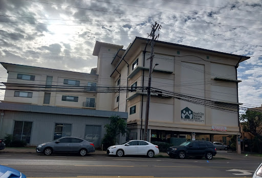 An urban scene featuring a multi-story building and parked cars against a cloudy sky.