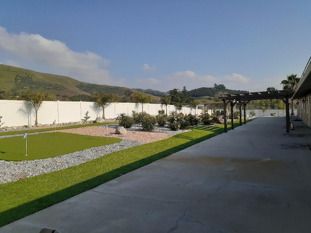 A scenic garden view with a pathway bordered by trees and distant mountains under a clear sky.